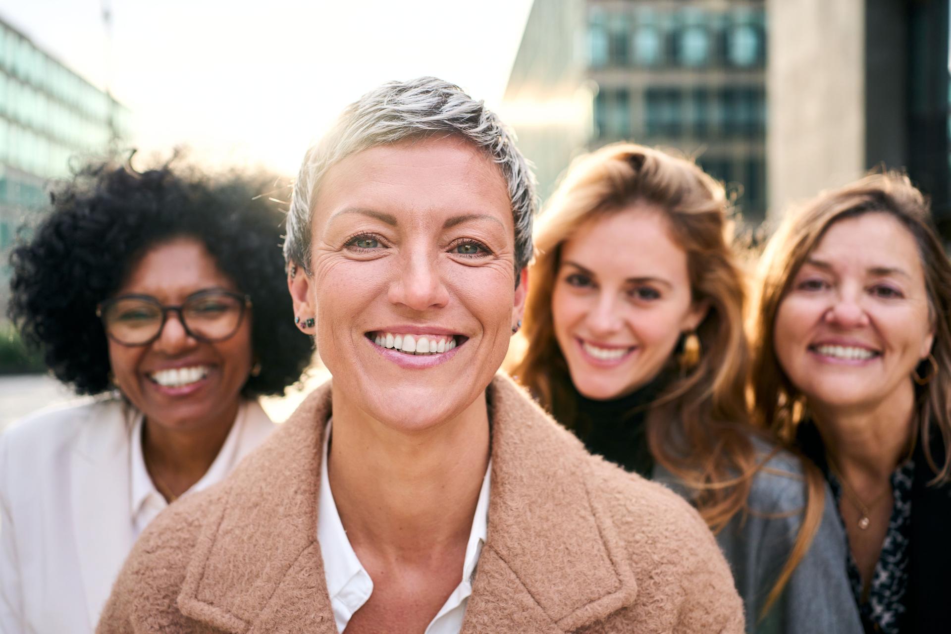 Portrait multiracial group empowered women of diverse ages looking smiling at camera outdoor.