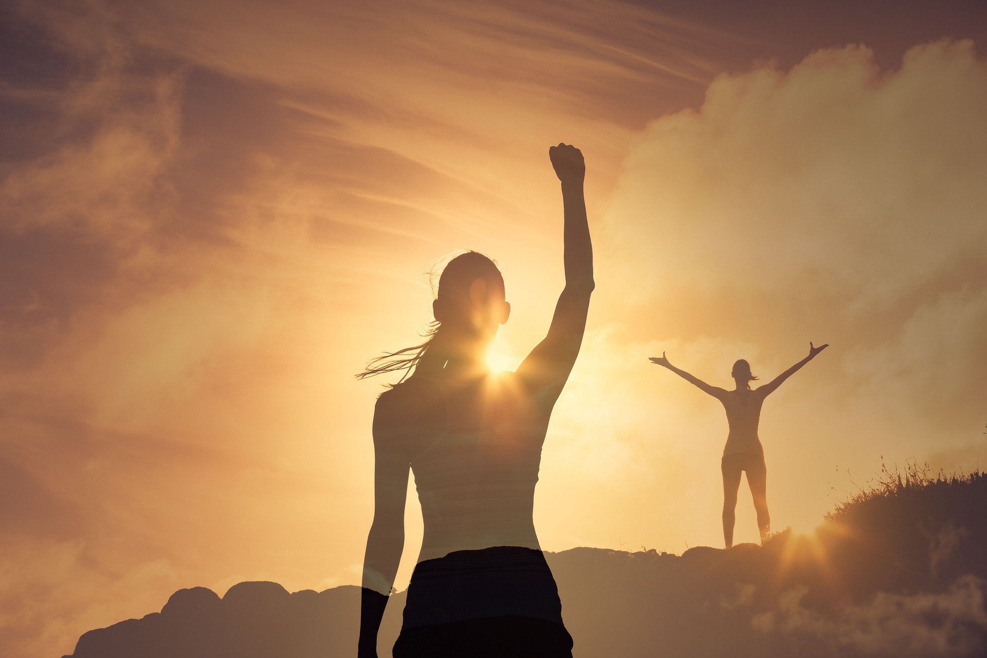 Strong young woman high on a mountain with fist up to the sky feeling inspired victorious.