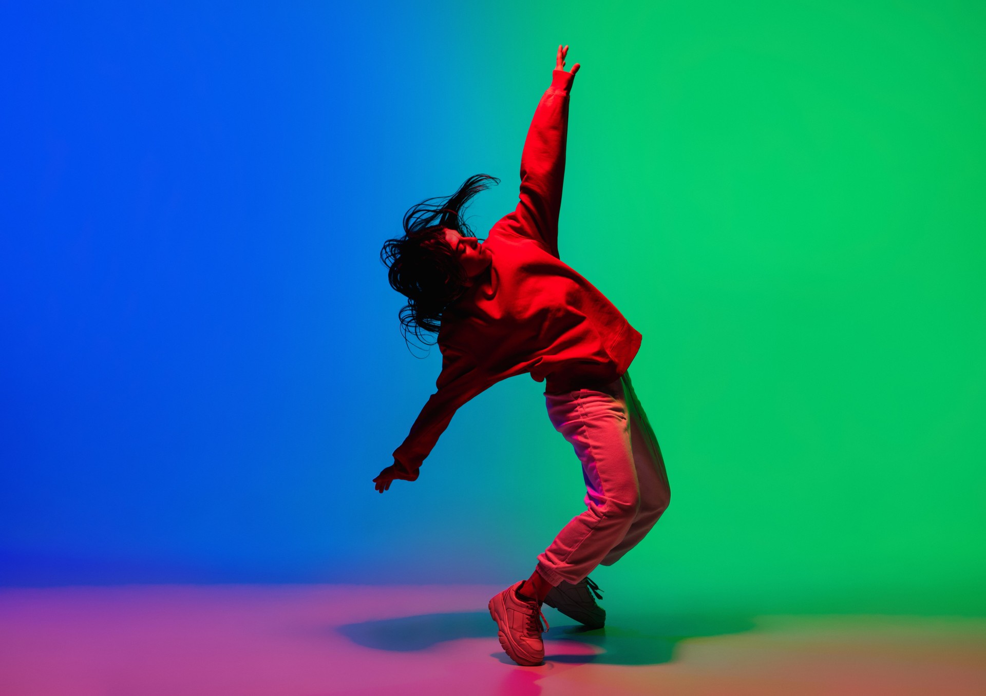 Stylish sportive girl dancing hip-hop in stylish clothes on colorful background at dance hall in neon light. Youth culture, movement, style and fashion, action.
