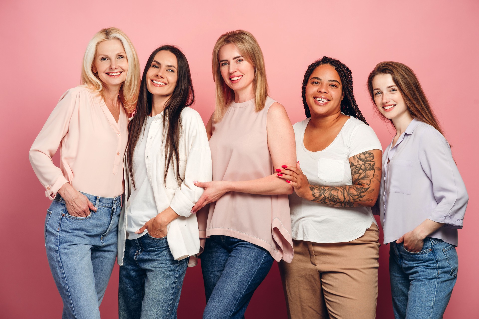 Five diverse women of different ages and ethnicities are smiling and posing together